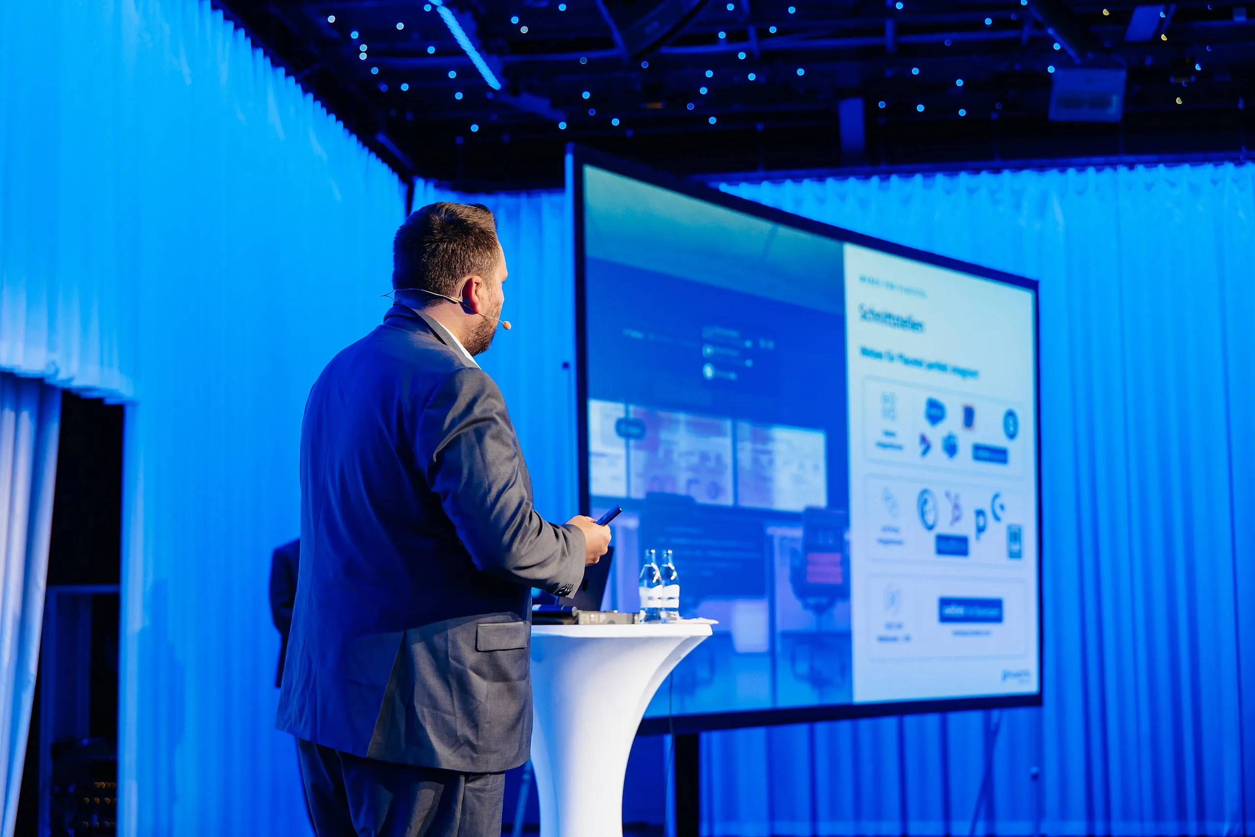Daniel Selbach als Keynote-Speaker auf blau beleuchteter Bühne, im Hintergrund eine Folie zu Schnittstellen
